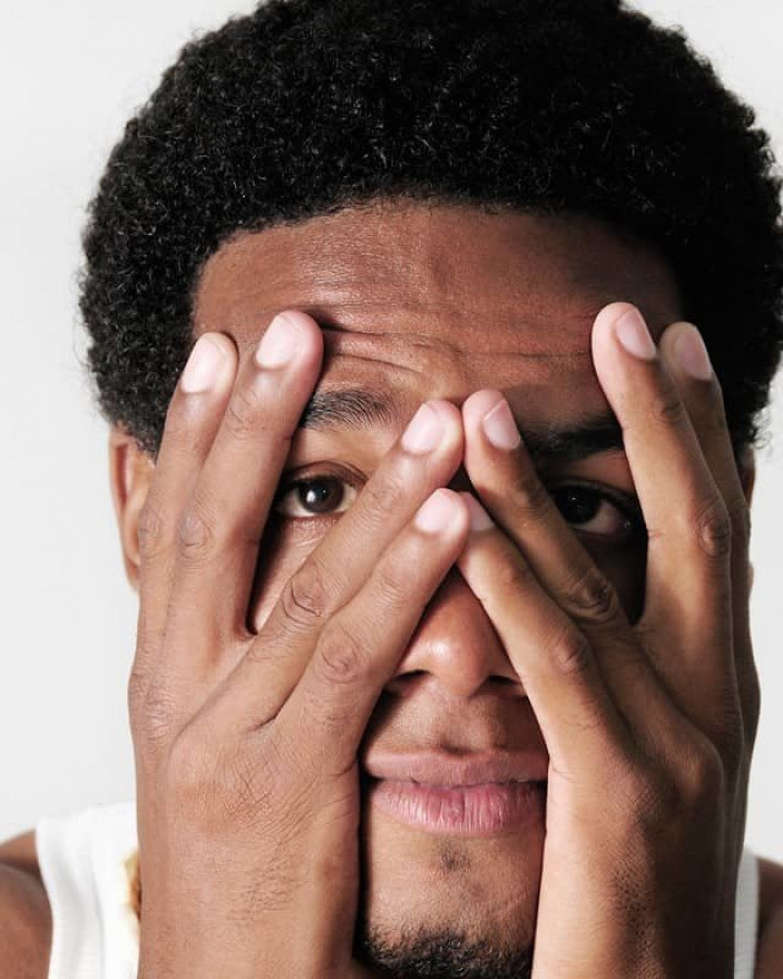picture of a black man hiding behind his hands due to fear