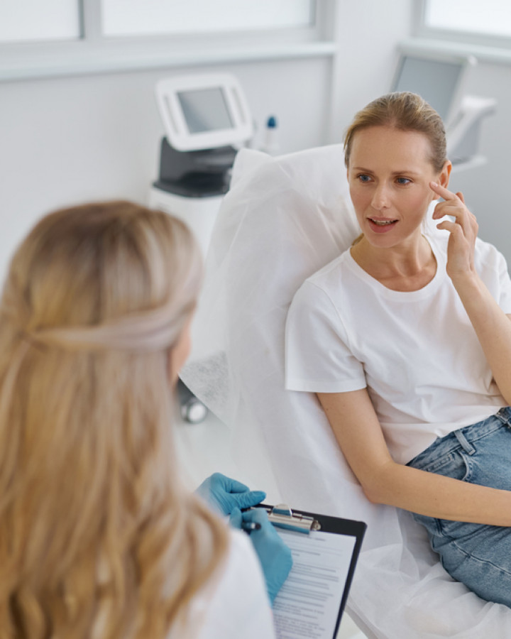 Female client pointing with fingers at wrinkles talking to doctor