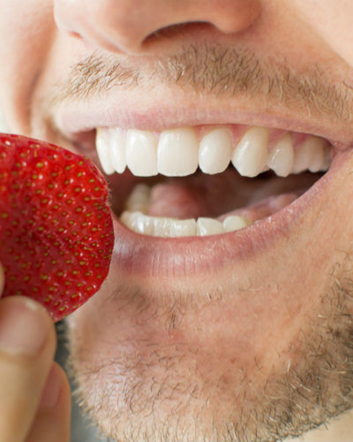 man with healthy white teeth biting into a strawberry due to dental care at orchard house northallerton
